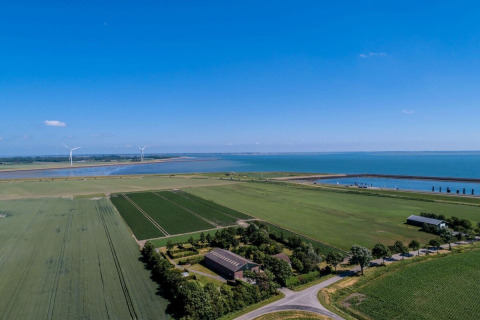 Luftfoto af Camping 'de Val' i Zeeland, Holland, med marker, havudsigt og vindmøller under en klar himmel.