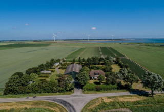 Vista aerea di Camping 'de Val' a Zeeland, Paesi Bassi, circondato da campi, pale eoliche e vista mare.