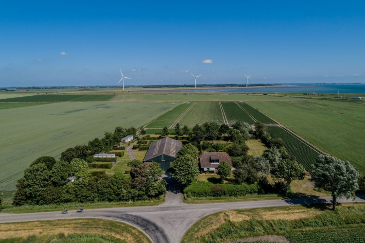 Aerial view of Camping 'de Val' holiday park in Zeeland, Netherlands, with fields, wind turbines and sea.