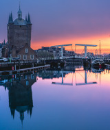 Sunset in Zierikzee, Netherlands, showing the historic tower, drawbridge, and reflections on calm water.