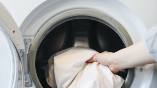 Una mano introduce ropa blanca en una lavadora de carga frontal en un alojamiento glamping en un parque vacacional.