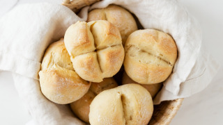 Cesta con panecillos recién hechos sobre un paño blanco, colocada en una superficie de mármol clara.