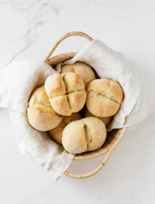 A basket of freshly baked bread rolls lined with a white cloth, set on a bright, marble countertop.