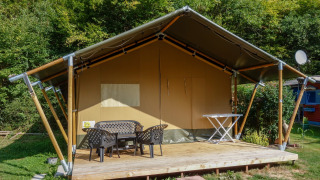 Tienda safari con terraza y muebles en Camping Bockenauer Schweiz en Alemania, rodeada de vegetación.
