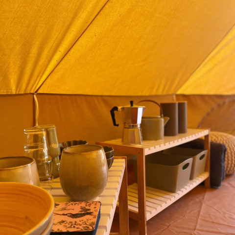 Interior de una tienda safari en Belltent, Camping Drei Spatzen, Alemania, con utensilios de cocina en estantes.