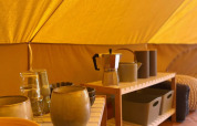 Inside a safari tent at Belltent, Camping Drei Spatzen, Germany, with dishes and kitchen items on shelves.