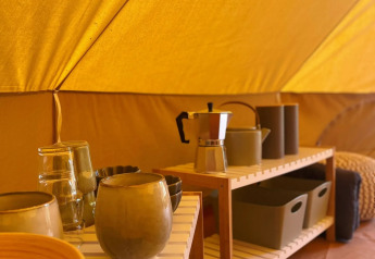 Interior de una tienda safari en Belltent, Camping Drei Spatzen, Alemania, con utensilios de cocina en estantes.