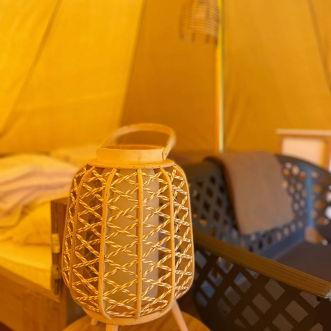 Interior de la tienda safari Belltent en Camping Drei Spatzen, Alemania, con farol de mimbre y silla moderna.