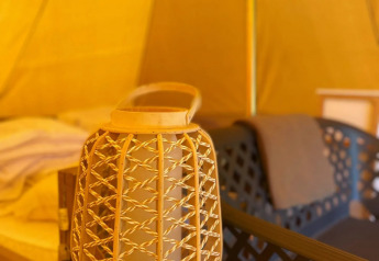 Interior de la tienda safari Belltent en Camping Drei Spatzen, Alemania, con farol de mimbre y silla moderna.