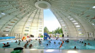 Piscina cubierta con techo abovedado y personas disfrutando en hu Birkelt Village, en Mersch, Luxemburgo.