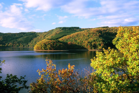 Vue sur un lac paisible entouré de collines boisées à hu Birkelt Village, parc de vacances à Mersch, Luxembourg.