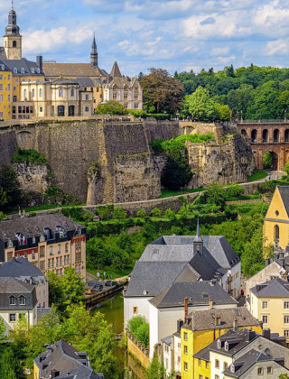 Vista panorámica de Larochette, Mersch, Luxemburgo, con casas coloridas y acantilados verdes bajo el cielo azul.