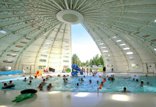 Indendørs swimmingpool med børn og voksne i svømning, under kuppelformet tag, hos hu Birkelt Village.
