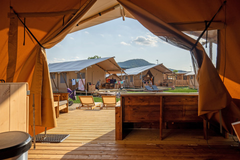 Vue depuis l'intérieur d'une tente safari avec terrasse en bois, chaises longues et autres tentes autour.