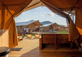 Vue depuis l'intérieur d'une tente safari avec terrasse en bois, chaises longues et autres tentes autour.