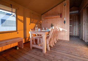 Interno di una tenda safari con arredi in legno, tavolo da pranzo e luce naturale calda e accogliente.