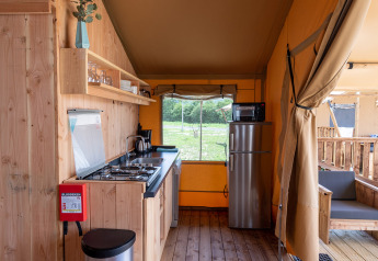 Moderne keuken in een safaritent met houten vloer, fornuis, koelkast en zicht op de buitenomgeving.