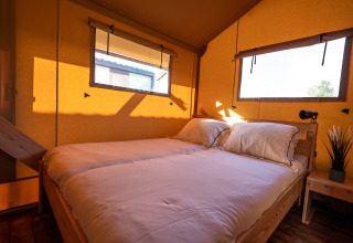 La luce del sole illumina una camera da letto in tenda safari con due letti e finestre ampie.