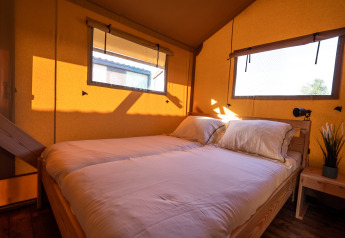 Luz natural entra en un dormitorio de tienda safari con dos camas, muebles de madera y grandes ventanas.