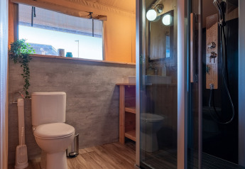 Modern bathroom in a safari tent with a toilet, glass shower, wood-look floors, and a large window.