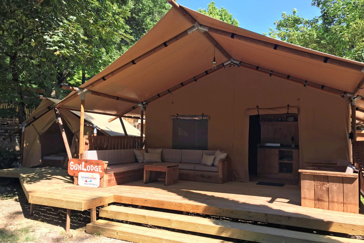 Safaritent SunLodge Taiga&Kambi met houten veranda, buitenbank en omgeven door groene bomen.