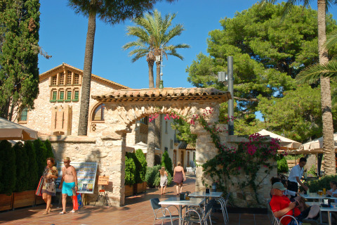 Outdoor scene at Camping Vilanova Park in Catalonia, Spain, featuring people, tables, and palm trees.