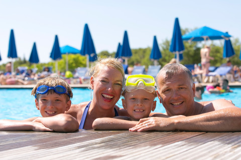 Famiglia felice in piscina al Camping Vilanova Park in Catalogna, Spagna, sorridendo durante una giornata di sole.