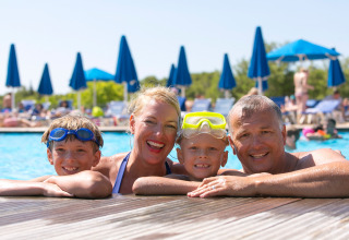 Famiglia felice in piscina al Camping Vilanova Park in Catalogna, Spagna, sorridendo durante una giornata di sole.