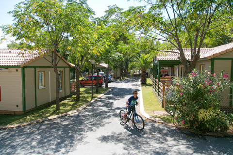 Niño monta una bicicleta entre bungalows y vegetación en Camping Vilanova Park, Cataluña, España.