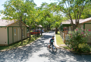 Barn cykler mellem hytter i Camping Vilanova Park, omgivet af grønne træer og bilfri veje i Spanien.