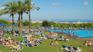 Gasten ontspannen aan het zwembad in Camping Vilanova Park met palmbomen en uitzicht op Catalonië, Spanje.