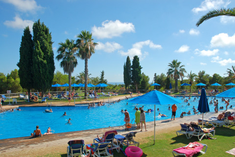 Piscina al aire libre con sombrillas, tumbonas y palmeras en Camping Vilanova Park en Cataluña, España.