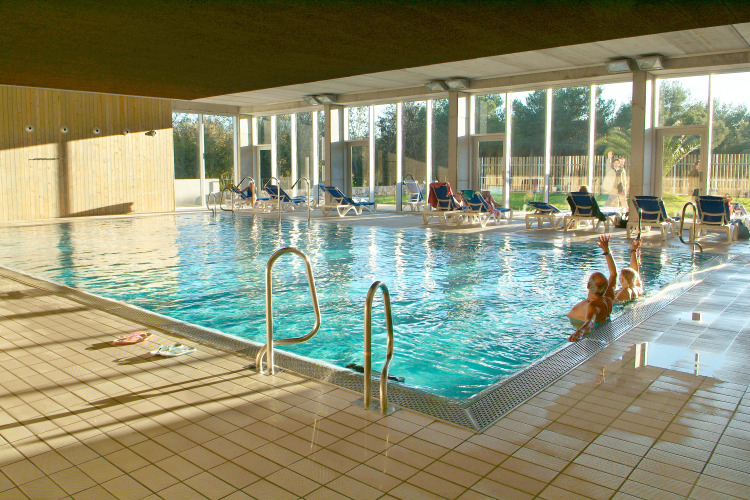 Piscine intérieure avec transats et grandes baies vitrées au Camping Vilanova Park, parc de vacances en Catalogne, Espagne.