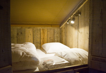 Cama acogedora con paredes de madera y ropa de cama dentro de una lujosa tienda de glamping en Bélgica.