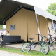 Niños juegan junto a una tienda safari glamping con bicicletas y muebles al aire libre en una terraza.
