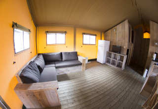 Interieur van een safari glamping tent met bank, koelkast en houten vloer bij Vakantiepark Klein Strand, België.