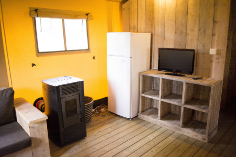Interieur van een safaritent met houten wanden, koelkast, tv, bank en kachel op Klein Strand in België.