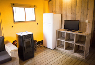 Interieur van een safaritent met houten wanden, koelkast, tv, bank en kachel op Klein Strand in België.