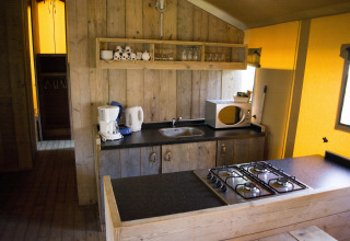 Cocina en una tienda safari Glamping en Vakantiepark Klein Strand, Bélgica, con estufa y microondas.