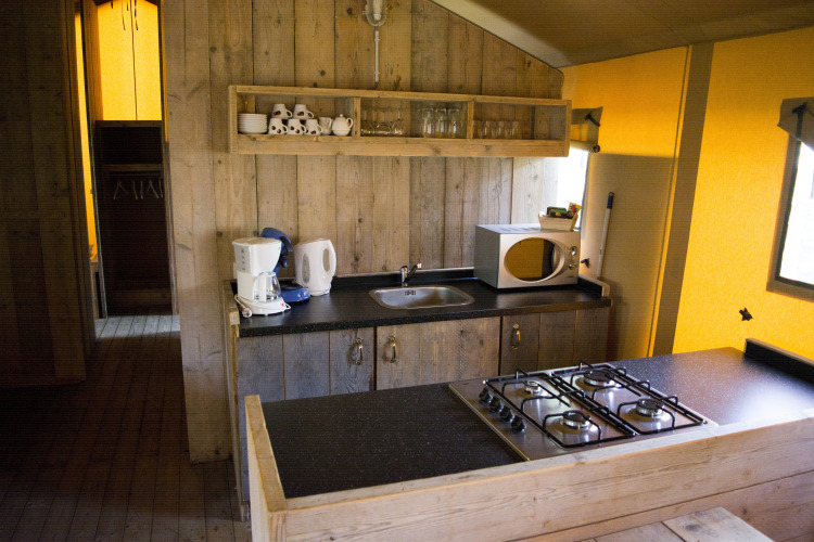 Cocina en una tienda safari Glamping en Vakantiepark Klein Strand, Bélgica, con estufa y microondas.