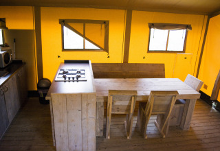 Interno di una tenda safari con mobili in legno e angolo cucina al Glamping di Vakantiepark Klein Strand, Belgio.
