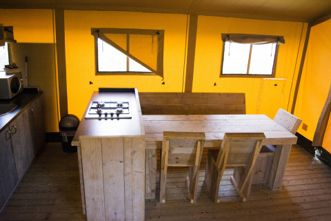 Interno di una tenda safari con mobili in legno e angolo cucina al Glamping di Vakantiepark Klein Strand, Belgio.