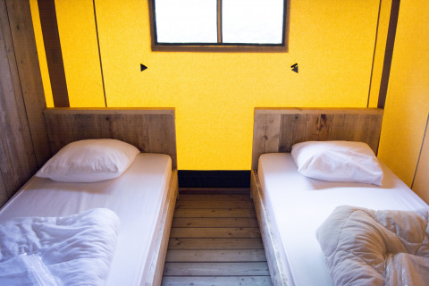 Twee eenpersoonsbedden in een safaritent met houten panelen en geel licht bij Vakantiepark Klein Strand, België.