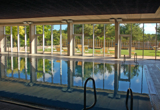Piscina cubierta con grandes ventanales y vistas al jardín en Camping Vilanova Park, Cataluña, España.