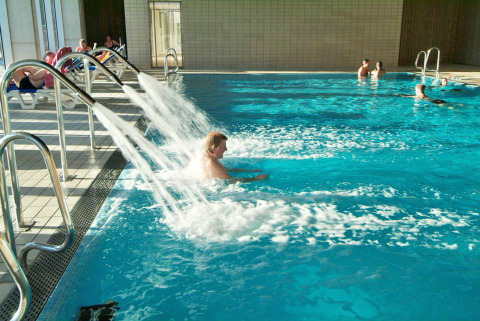 Piscina coperta con ospiti che si rilassano sotto i getti d’acqua al Camping Vilanova Park in Catalogna, Spagna.