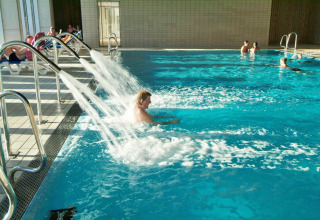 Piscina coperta con ospiti che si rilassano sotto i getti d’acqua al Camping Vilanova Park in Catalogna, Spagna.
