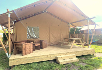 Safari telt Glamping med overdækket træterrasse, træmøbler og picnicbord i solrige omgivelser.