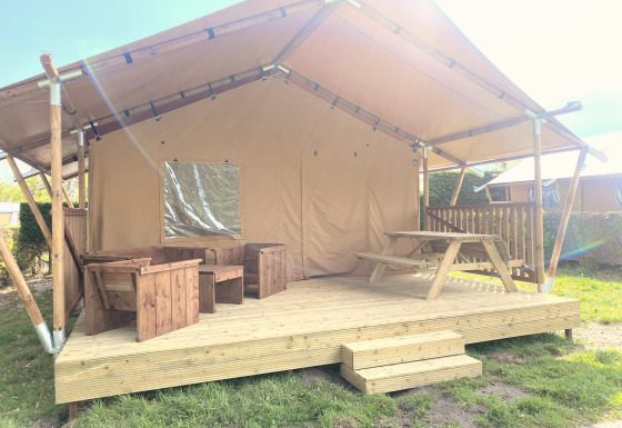 Safari-Zelt Glamping mit überdachter Holzterrasse, Holzmöbeln und Picknicktisch bei Sonnenschein.