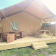 Tienda safari Glamping con terraza de madera cubierta, muebles de exterior y mesa de picnic al sol.