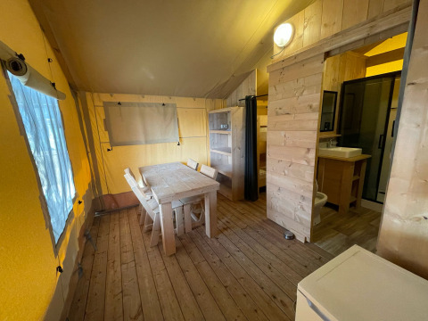 Interior of a safari tent with wooden furniture, dining table, kitchen, and bathroom at Glamping Klein Strand.